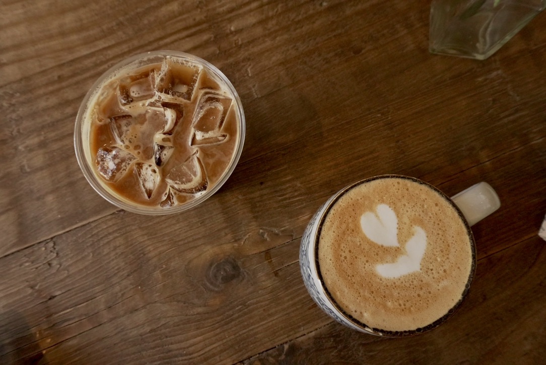 Dos cafecitos sobre una mesa de madera: uno helado y un flat white