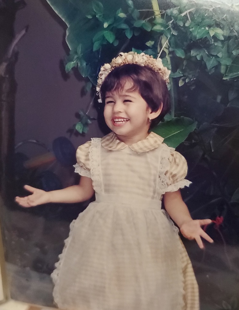 Annette de niña, riéndose, con una corona de flores y un vestido claro